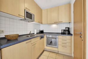 Una cocina con armarios de madera, microondas, cafetera y lavavajillas.