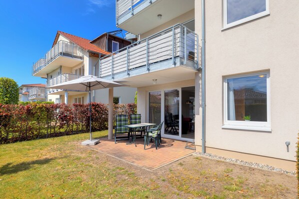 A two-story building with balconies, a patio with a table and chairs, and a garden area.