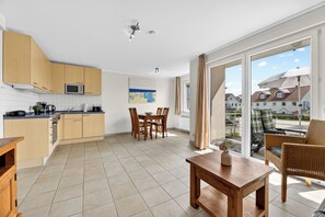 A modern kitchen with wooden cabinets, a dining area with a table and chairs, and a balcony with a view of the neighborhood.