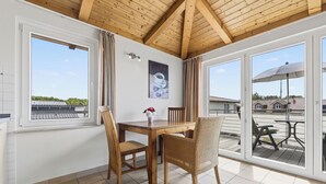 A room with a wooden ceiling, a dining table with chairs, a window with curtains, and a view of the outside. - Am Sonnenblick Whg. 5: Apartment with balcony near the sandy beach in Heringsdorf (Heringsdorf)