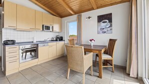 A kitchen with wooden cabinets, a microwave, an oven, and a dining area with a table and chairs. - Am Sonnenblick Whg. 5: Apartment with balcony near the sandy beach in Heringsdorf (Heringsdorf)