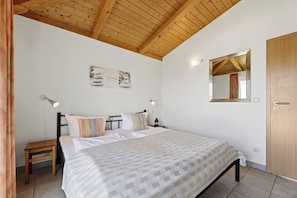 A bedroom with a wooden ceiling, a bed with patterned bedding, a nightstand with a lamp, and a wall-mounted mirror.