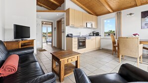 A modern living room with a TV, leather sofa, wooden coffee table, and a kitchen with wooden cabinets and a microwave. - Am Sonnenblick Whg. 5: Apartment with balcony near the sandy beach in Heringsdorf (Heringsdorf)
