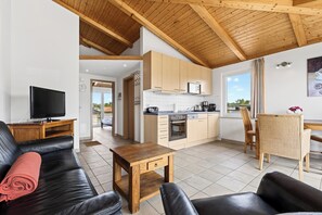 A modern living room with a TV, leather sofa, wooden coffee table, and a kitchen with wooden cabinets and a microwave.