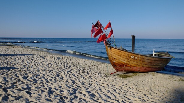 A wooden boat with red flags on a sandy beach by the sea. - Am Sonnenblick, Whg. 6:41 m² apartment with balcony, WLAN & close to the beach (Heringsdorf)