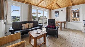 A spacious living area with a wooden ceiling, a black leather sofa, a dining table, and a chair. - Am Sonnenblick, Whg. 6:41 m² apartment with balcony, WLAN & close to the beach (Heringsdorf)