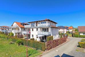 A residential building with multiple balconies, a paved driveway, and a well-maintained garden.