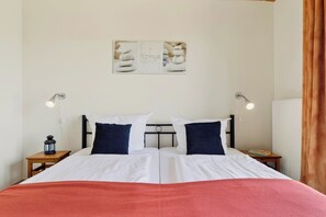 A neatly made bed with white and red bedding, two bedside lamps, a nightstand with a lantern, and a wall-mounted picture frame.