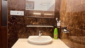 Une salle de bain avec un lavabo blanc, un miroir, un porte-serviettes et une bouteille de shampoing verte.