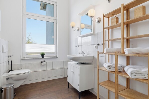 Un baño moderno con inodoro, lavamanos y estantes de madera con toallas.