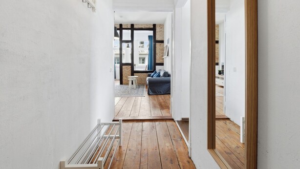 Un couloir étroit, doté d’un plancher en bois, mène à un espace de vie comprenant un canapé et une table basse.
