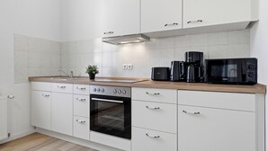 Une cuisine moderne avec des meubles blancs, un four encastré, un four à micro-ondes et une machine à café.