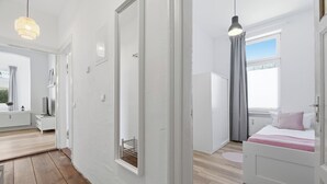 Une chambre d’hôtel moderne avec un plancher en bois, un lit recouvert d’une courtepointe rose et blanche, une fenêtre donnant sur un beau paysage et une porte blanche.