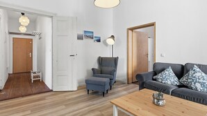 Une pièce avec un plancher en bois, un canapé gris, une petite table, une chaise et un luminaire au plafond.