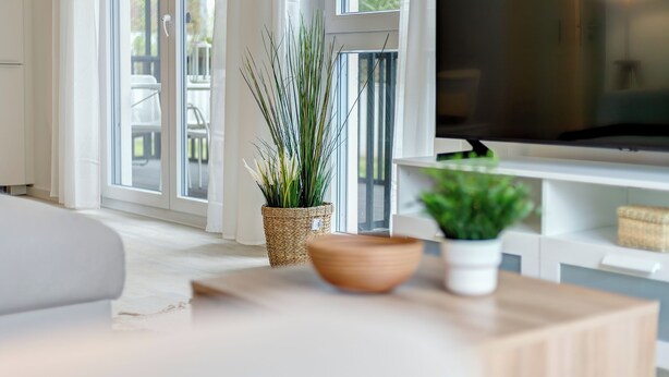 Un salon moderne doté d’une grande fenêtre, d’un téléviseur à écran plat, d’une table basse en bois et de deux plantes en pot.