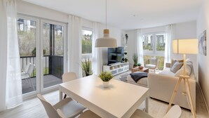 Un salon moderne avec un canapé blanc, une table à manger et un téléviseur posé sur un meuble en bois.