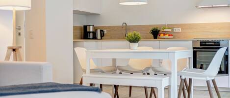A modern kitchen with white cabinetry, a dining table with chairs, and a built-in oven.