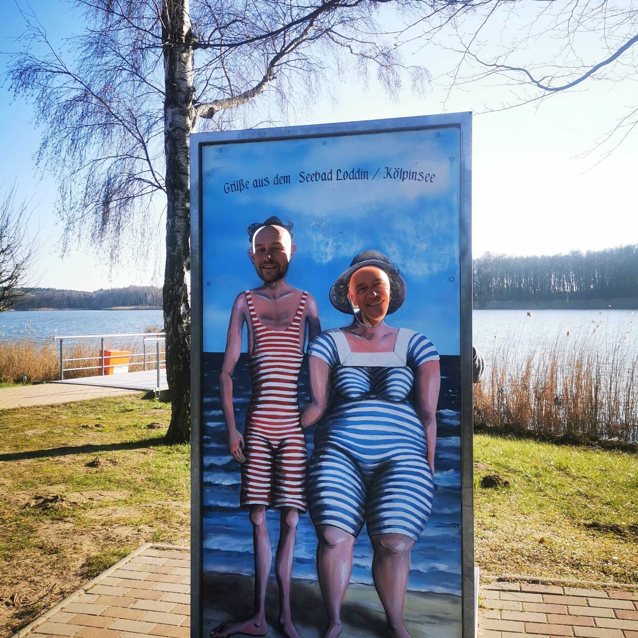 A sign with two figures, one in a striped swimsuit and the other in a hat, standing by a lake.