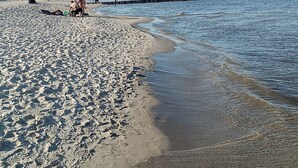 Une plage avec une jetée en bois qui s’avance dans l’eau, un rivage sablonneux et un ciel dégagé.