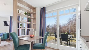 A dining area with a table and chairs, a bookshelf, and a view through a glass door.