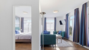 A modern hotel room with a bed, a green sofa, a TV, and a large window with curtains.