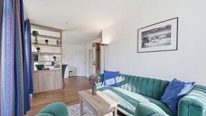 A modern living room with a green sofa, a wooden coffee table, and a kitchen area in the background.
