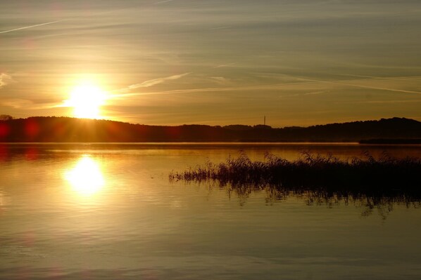 A calm lake at sunset with a silhouette of trees and a distant hill. - Regina Maris Apartment 106 with a terrace, Wi-Fi, and just 100 meters from the sandy beach (Bansin)