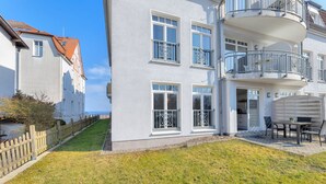 Un edificio de varios pisos con balcones, un patio con mobiliario exterior y un cielo despejado.