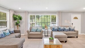 A spacious living room with a large window, two sofas, a coffee table, and a potted plant. - These units are in the highly sought after Pensacola Heights neighborhood. (Pensacola)