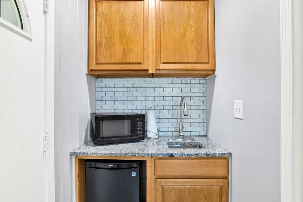 A compact kitchen with wooden cabinets, a microwave, a dishwasher, and a tiled backsplash.