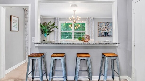 A kitchen with a central island, three stools, a chandelier, and a window with green shutters. - These units are in the highly sought after Pensacola Heights neighborhood. (Pensacola)