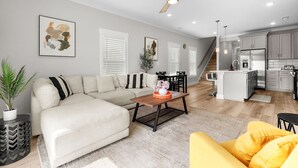 A modern living room with a sofa, a coffee table, and a dining area with chairs. There is a kitchen with cabinets and a refrigerator. - Luxury waterfront retreat-Near golf Beach Barefoot (Longs)