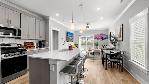 A modern kitchen with a central island, stainless steel appliances, and a dining area with a table and chairs. - Luxury waterfront retreat-Near golf Beach Barefoot (Longs)
