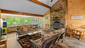 A cozy cabin interior with a stone fireplace, wooden furniture, and large windows offering a view of the forest. - Peaceful 3BR*Firepit*Games*8 Mins to National Park (Cosby)