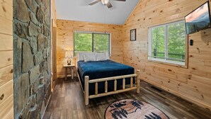 A wooden cabin bedroom with a bed, a ceiling fan, and two windows. - Peaceful 3BR*Firepit*Games*8 Mins to National Park (Cosby)