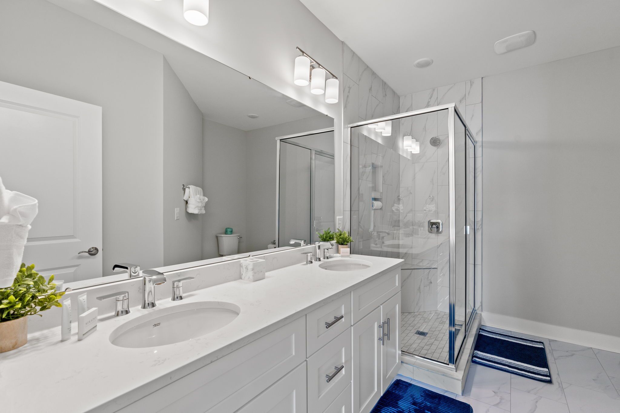 A modern bathroom with two sinks, a large mirror, and a glass-enclosed shower.