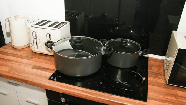 Une cuisine avec un plan de travail en bois, un grille-pain, une bouilloire et deux casseroles sur une plaque de cuisson à induction.