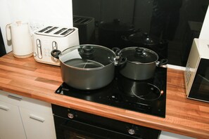 A kitchen with a wooden countertop, a toaster, a kettle, and two pots on an induction cooktop. - EEE HOMES WOLVERHAMPTON: A pleasant 3-bedroom house with WiFi. (Wolverhampton)
