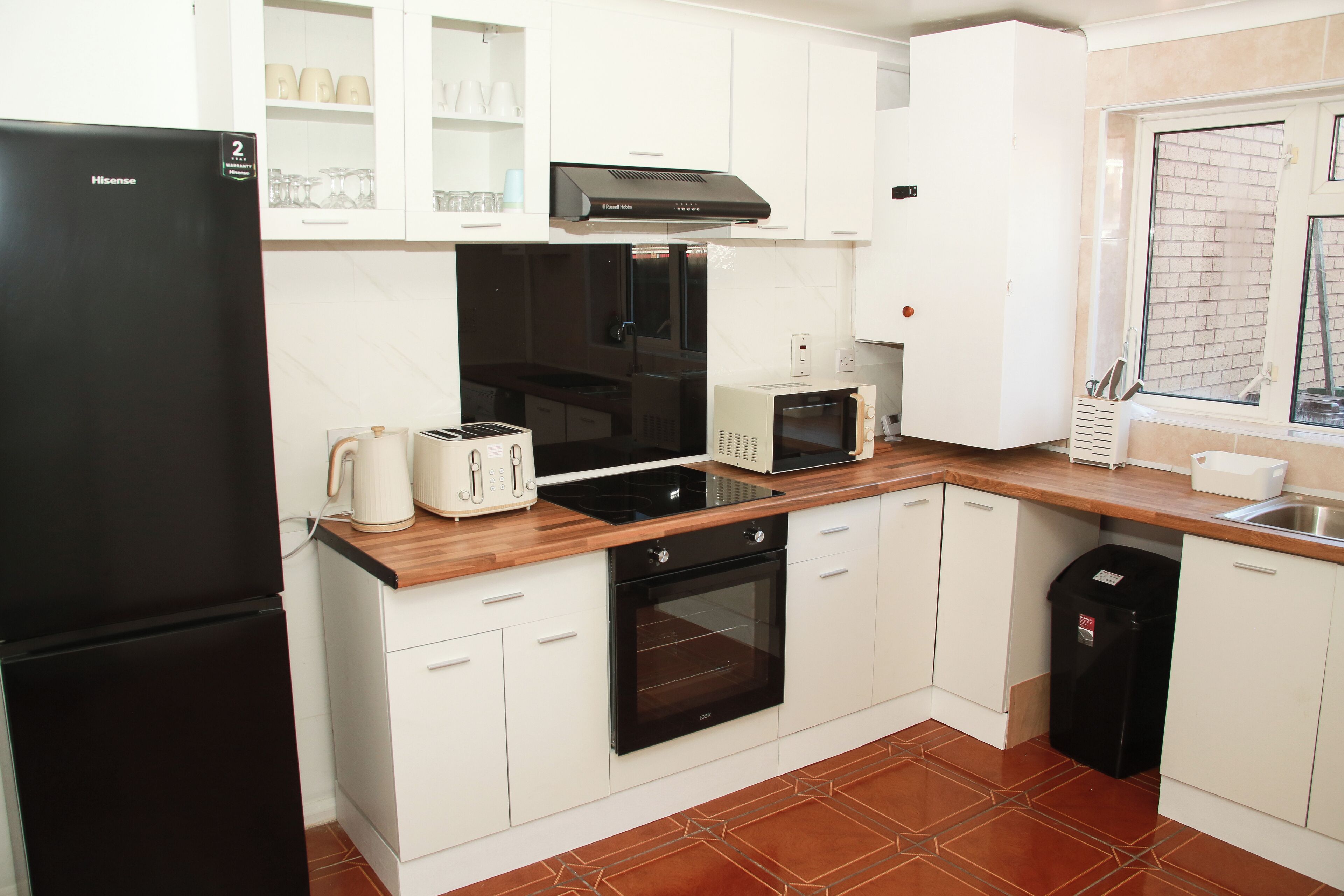 A compact kitchen with white cabinets, a black refrigerator, a microwave, a toaster, and an oven.