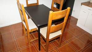 Une table à manger avec quatre chaises en bois, une nappe noire et un sol carrelé.