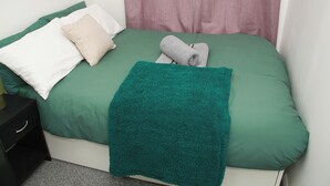 Un lit avec une literie verte, un plaid turquoise et deux serviettes enroulées.