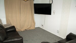 Un salon doté d’un téléviseur à écran plat fixé au mur, de deux canapés en cuir, d’un rideau beige et d’un sol recouvert de moquette.
