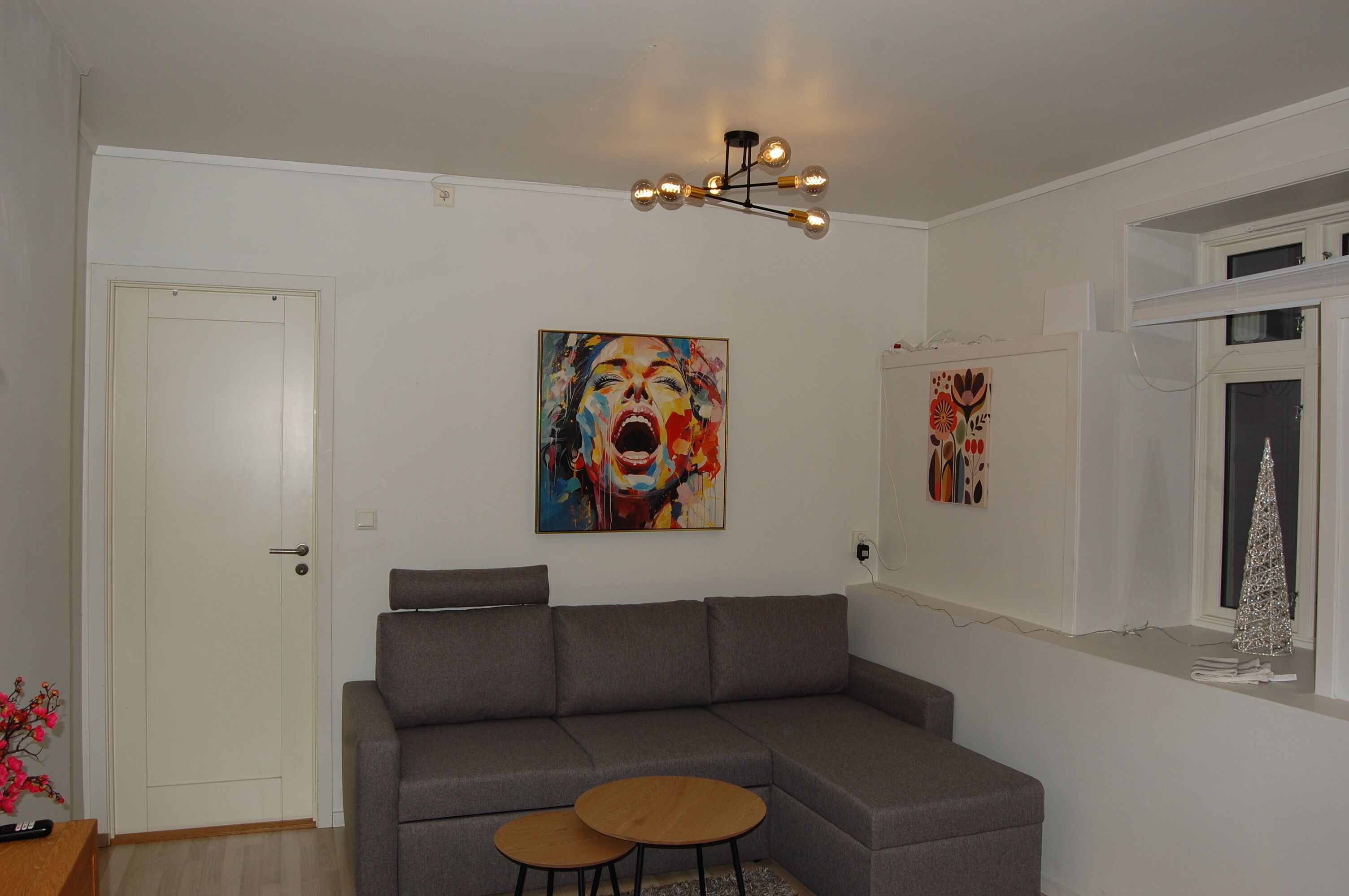 Ein modernes Wohnzimmer mit einem grauen Ecksofa, zwei kleinen runden Tischen und einem farbenfrohen abstrakten Gemälde an der Wand.