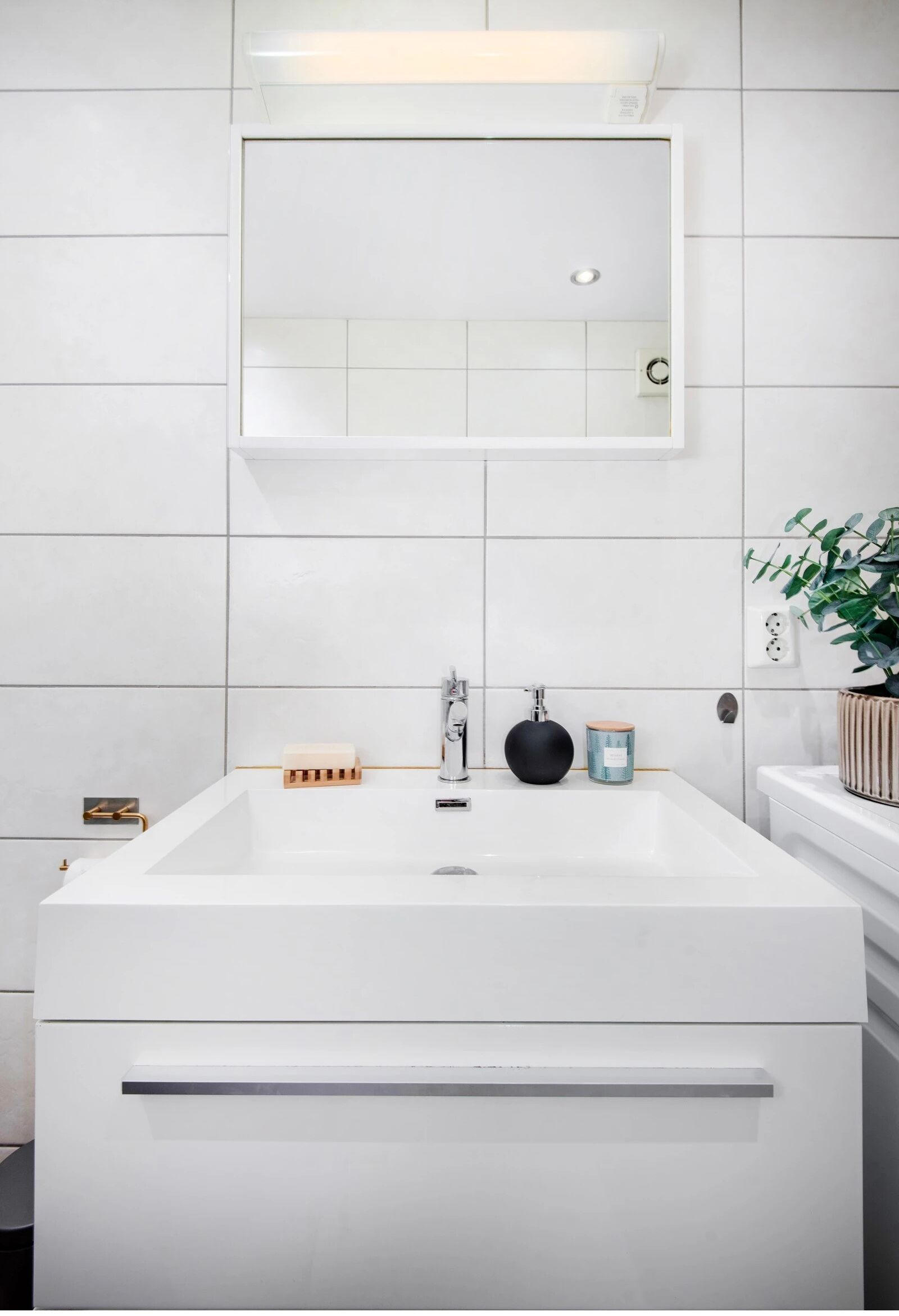Ein modernes Badezimmer mit einem großen, weißen Waschbecken, einem Spiegel darüber und einer Zimmerpflanze rechts.