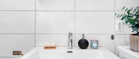A modern bathroom with a large white sink, a mirror above it, and a potted plant on the right.