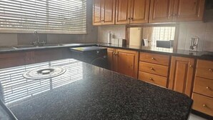 Une cuisine dotée de plans de travail en granit, de meubles en bois et d’une fenêtre avec des stores.
