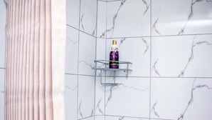 Une salle de bain aux carreaux de marbre blanc, un flacon de shampoing de la marque LUX posé sur une étagère en métal, et un rideau rose.
