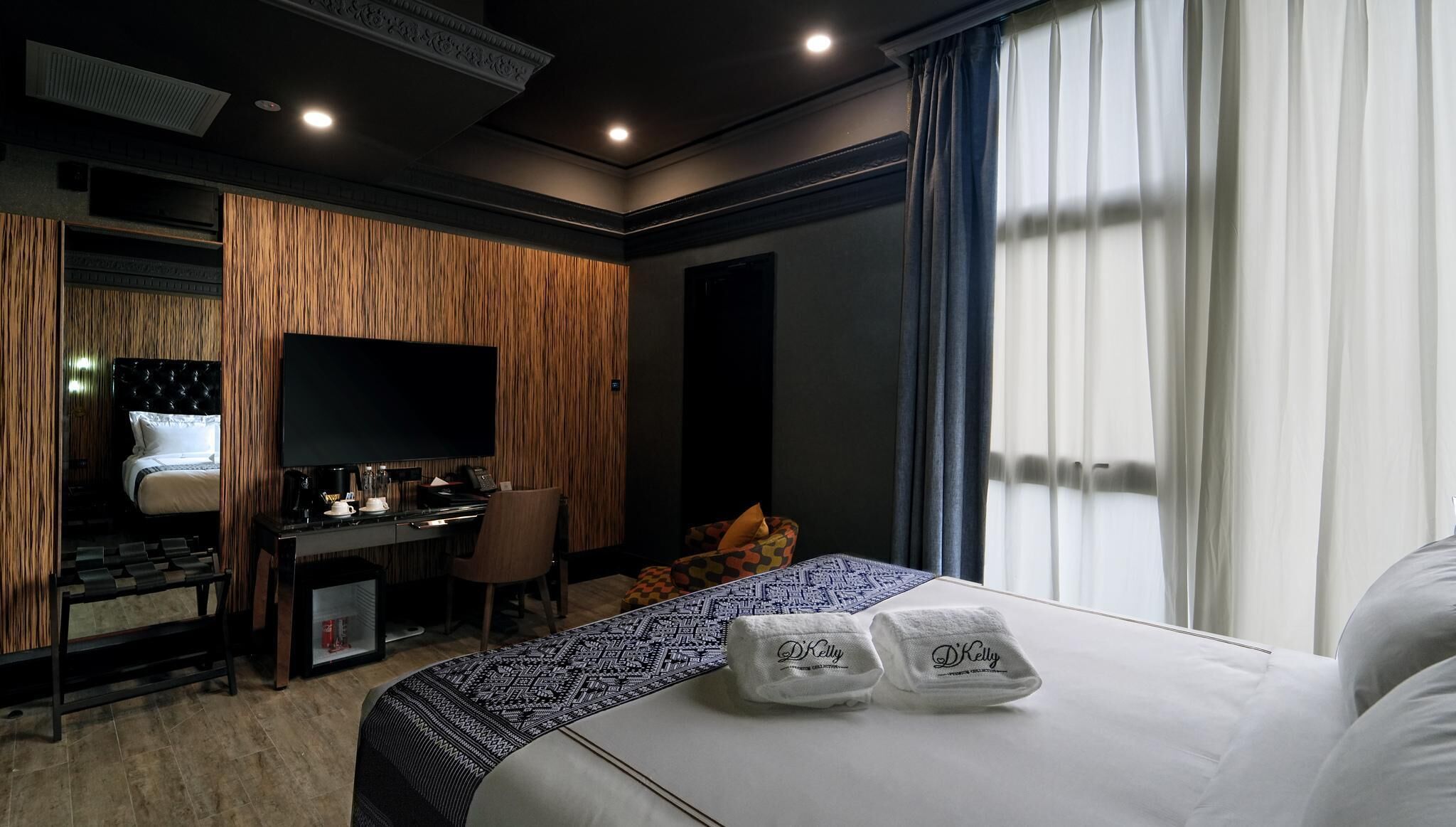 Une chambre d’hôtel équipée d’un lit, d’un bureau, d’une chaise, d’une télévision et d’une fenêtre avec des rideaux.