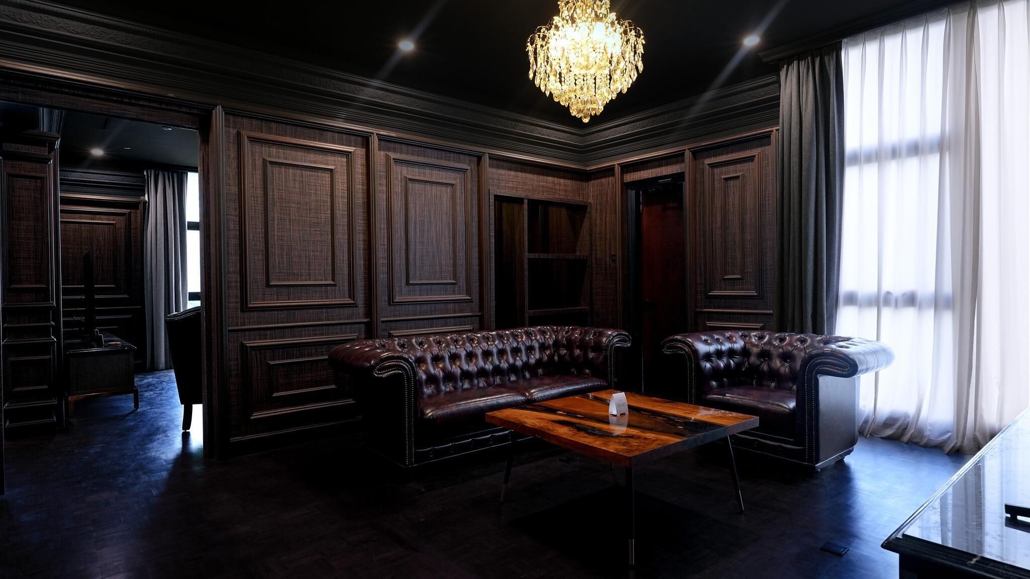 Um quarto com painéis de madeira escura, um sofá de couro e uma mesa de centro de madeira, além de um candelabro.