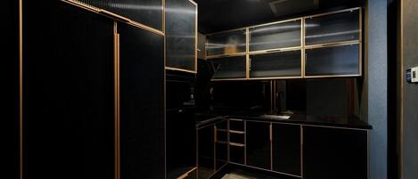 A modern kitchen with black cabinetry and gold accents, featuring a built-in oven and a sink.
